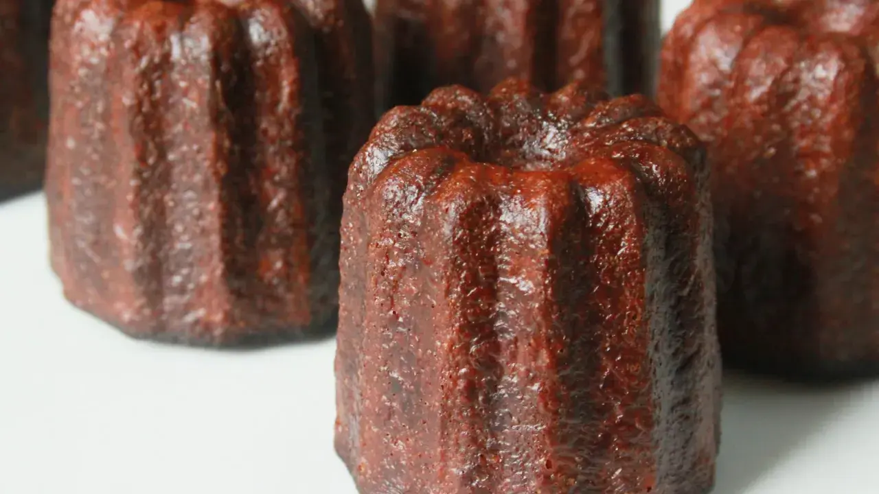 Plusieurs cannelés dorés, tout juste sortis du four, prêts pour la dégustation. La cuisson des cannelés révèle leur croûte caramélisée.