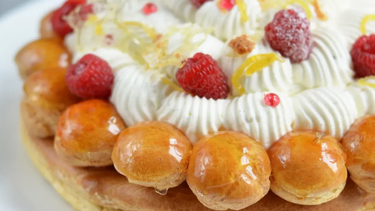 Un déliceux saint honoré framboise, orné de crème fouettée, de fruits rouges et de petites brioches caramélisées.