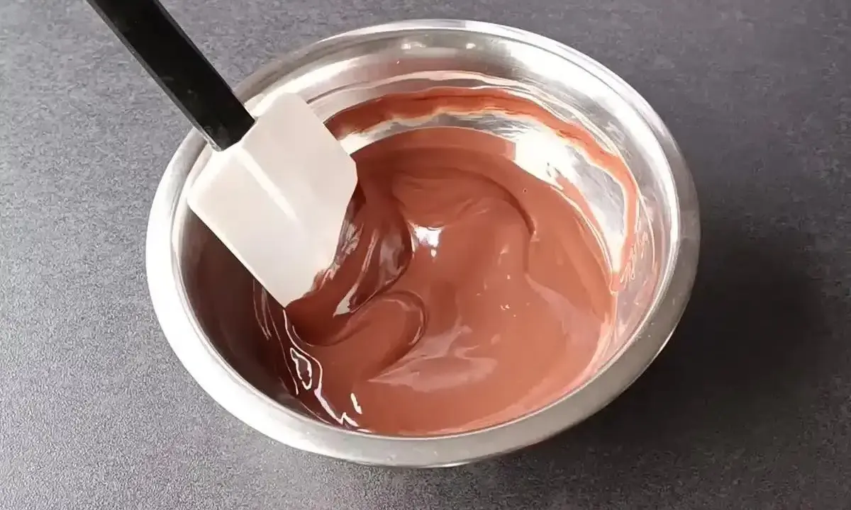 Une spatule mélange une ganache chocolat onctueuse dans un bol en métal.