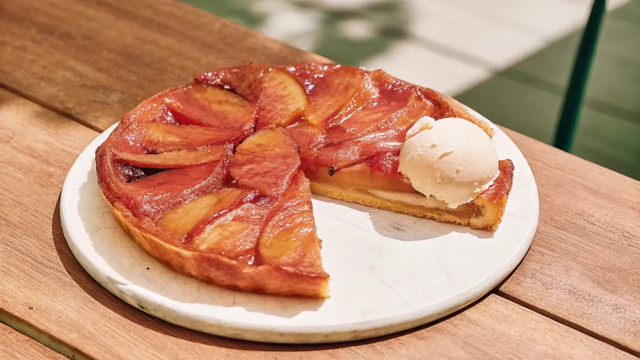 Tarte Tatin caramélisée, une part coupée, servie avec une boule de glace à la vanille. La cuisson parfaite révèle des pommes dorées et une pâte croustillante.