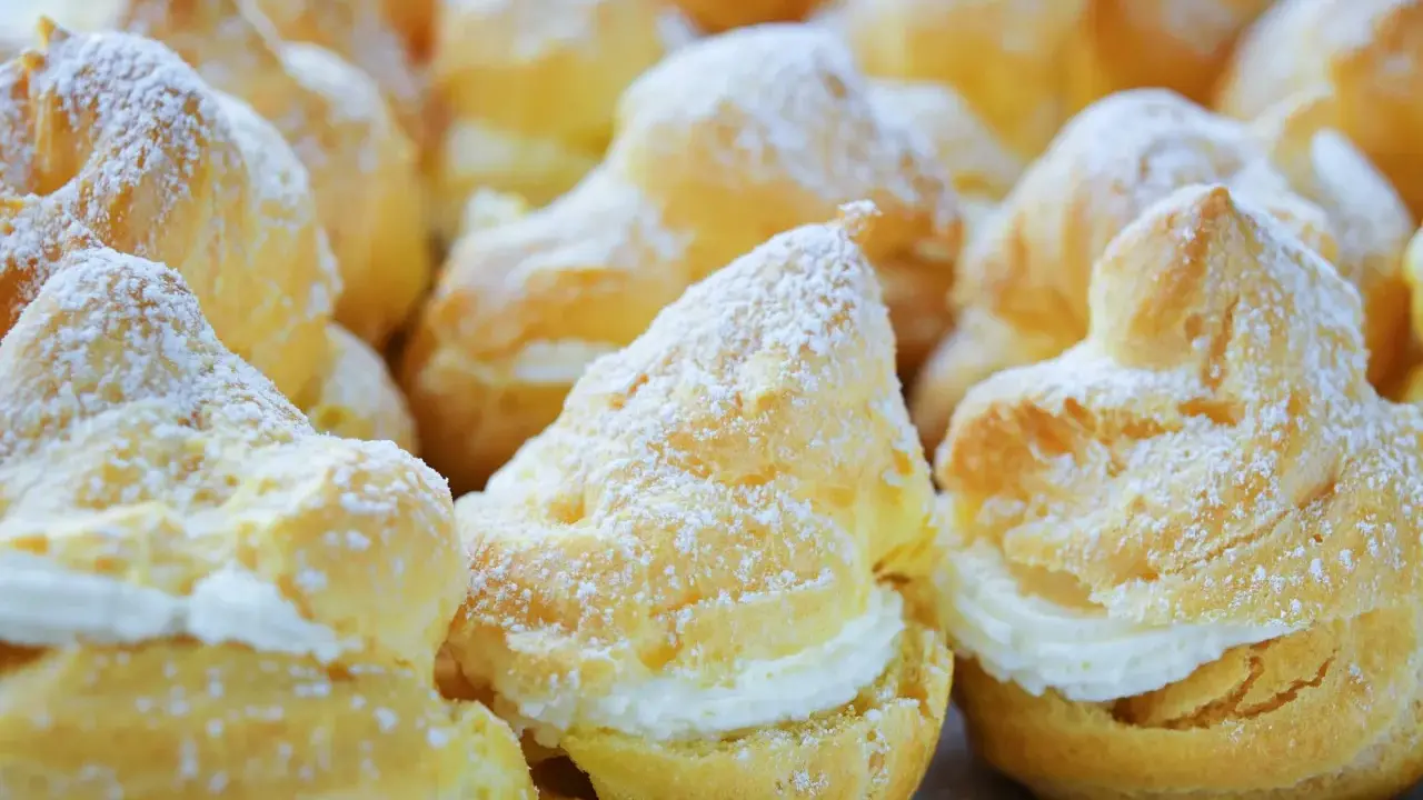 Une assiette de choux à la crème, saupoudrés de sucre glace. Ces petites merveilles de pâtisserie sont prêtes à être dégustées.