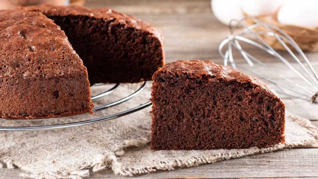 Un délicieux gâteau génoise chocolat, moelleux et aéré, prêt à être dégusté. Des ingrédients frais comme des œufs et du cacao sont visibles en arrière-plan.