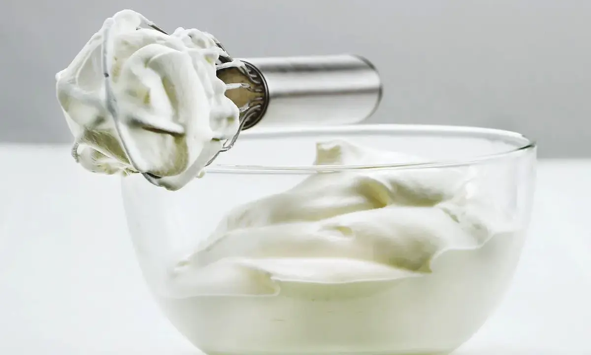 Crème fouettée aérienne prête à garnir un gâteau, dans un bol en verre.