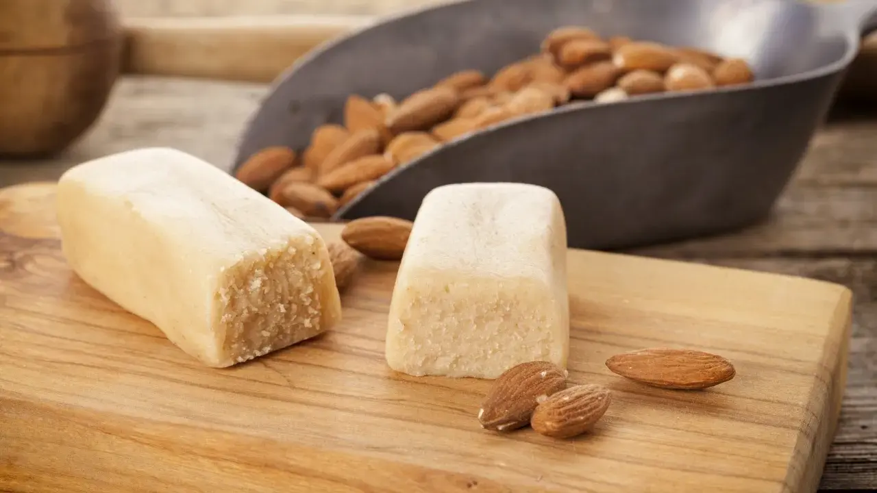 Deux blocs de pâte d'amande et des amandes dans une pelle, prêts pour une recette de pâte d'amande maison.