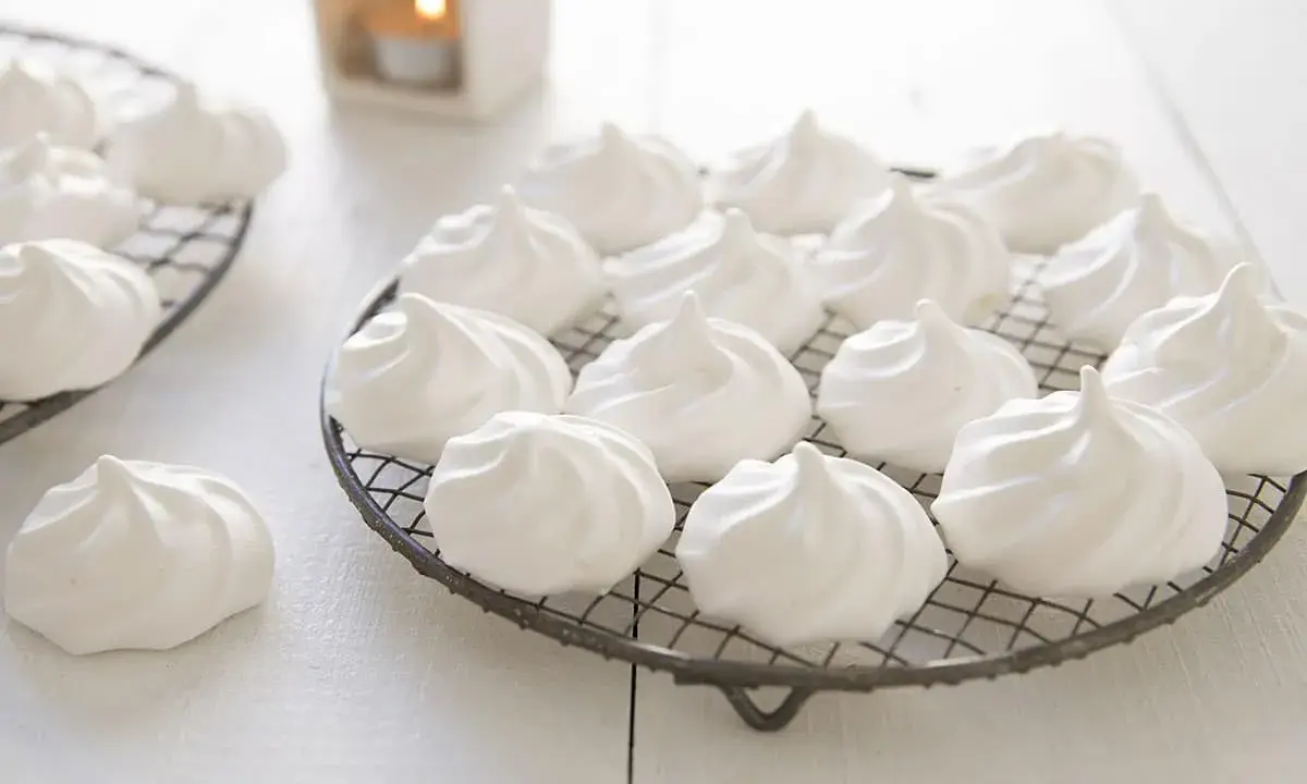 Douces meringues blanches, prêtes pour la cuisson. Elles reposent sur des grilles, évoquant la douceur et la légèreté.