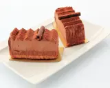 Deux parts de gâteau Trianon, le meilleur pâtissier, saupoudrées de cacao, sur une assiette blanche.