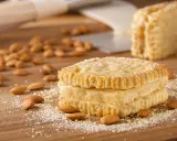 Trois biscuits joconde empilés, saupoudrés de sucre glace, entourés d'amandes sur une planche en bois.