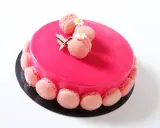 Entremet fraise rose vif, décoré de macarons roses et de petites fleurs blanches.