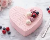 Un délicieux gâteau cœur rose, décoré de fruits rouges et de meringues, prêt à être dégusté.