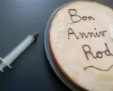 Glaçage pour écrire sur un gâteau : "Bon Anniv Rod". Une seringue est à côté, prête pour la décoration.