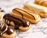 Plusieurs éclairs gourmands, certains au fondant chocolat noir, d'autres au glaçage caramel ou blanc, sur fond marbré.