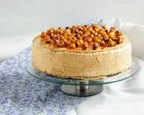 Gâteau dacquoise noisette garni de noisettes caramélisées sur un présentoir en verre.