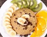 Un délicieux bowl cake flocon d'avoine garni de rondelles de banane, de tranches de kiwi et d'orange, parsemé de pépites de chocolat.