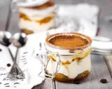 Deux bocaux de tiramisu, le meilleur dessert, saupoudrés de cacao, avec des grains de café et des cuillères sur une nappe en dentelle.