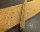 Deux fines tranches de biscuit moelleux noisette, parsemées de petits grains, reposent sur une surface sombre.