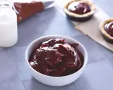 Un bol de ganache chocolat au lait onctueuse, prêt à garnir des tartelettes. Du lait et une poche à douille sont à proximité.