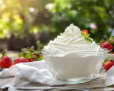 Un bol de crème chantilly qui tient longtemps, garni d'une fraise et d'une feuille de menthe, entouré de fraises fraîches.