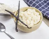 Un bol de riz au lait crémeux, garni de gousses de vanille, avec du riz brut à côté.