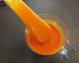 Une spatule verse un glaçage miroir orange vif dans un récipient en verre.