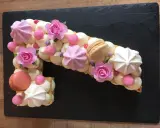 Un biscuit joconde number cake en forme de 1, décoré de crème, meringues, macarons et roses en sucre.