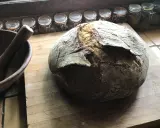 Gros pain artisanal sur une planche en bois, avec un mortier à côté. La question "peut on mélanger levain et levure" plane dans l'air.