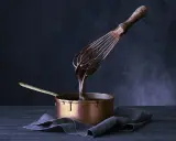 Sauce chocolat qui ne fige pas, coulante et brillante, dégouline d'un fouet dans une casserole en cuivre.
