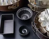 Collection de moules à gâteaux de différents types, certains en métal argenté, d'autres en métal noir, prêts pour la pâtisserie.