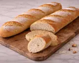Deux baguettes dorées, tout juste sorties du four, reposent sur une planche en bois. Une est coupée en tranches, révélant une mie aérée.