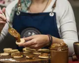 Une main dépose une cuillère de dulce de leche sur un biscuit rond, préparant des **caras crakine fait maison**.