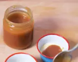 Un pot de caramel beurre salé sans beurre demi sel, prêt à être dégusté. Une cuillère est sur le point de plonger dans une petite coupelle de crème et de caramel.