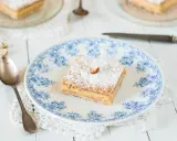 Un carré de gâteau russe, saupoudré de sucre glace et garni d'une noisette, sur une assiette ornée de bleu.