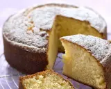 Un délicieux gâteau sans oeuf, saupoudré de sucre glace, attend sur une grille. Une part est déjà coupée, révélant sa mie moelleuse.