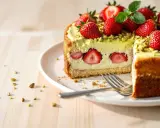 Gâteau fraisier pistache, garni de fraises fraîches et de pistaches concassées. Une part est coupée, révélant des rondelles de fraises à l'intérieur.