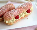 Deux éclairs à la framboise, garnis de crème légère et de fruits rouges, saupoudrés de sucre glace.