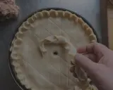 Main d'un pâtissier décorant une tarte avec une pâte brisée tressée. Un tas de farce est visible à gauche.