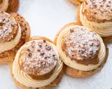 Plusieurs Paris-Brest, des pâtisseries rondes à la pâte à choux garnies de crème onctueuse et saupoudrées de sucre glace et d'amandes.