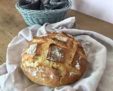 Un pain artisanal doré, prêt à être dégusté après son temps de pousse. Une corbeille de serviettes grises est visible en arrière-plan.