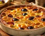 Un délicieux clafoutis aux pruneaux, doré et moelleux, sort du four. Des fruits entiers et coupés parsèment la pâte onctueuse.