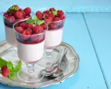 Trois panna cotta onctueuses, garnies de framboises fraîches et d'un coulis de framboise, sur un plateau argenté.