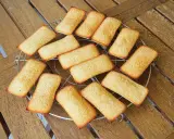 Douze biscuits financiers dorés, disposés sur une grille de refroidissement, sur une table en bois.
