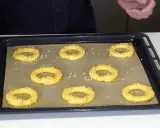 Huit ronds de pâte à choux, prêts à devenir un délicieux Paris-Brest, sont saupoudrés d'amandes effilées sur une plaque de cuisson.