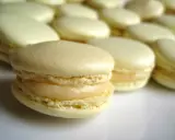 Un macaron meringue italienne, délicatement garni, se tient au premier plan, entouré d'autres douceurs pâles.