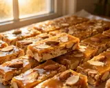 Des barres de nougatine aux amandes, dorées et brillantes, disposées près d'une fenêtre ensoleillée.