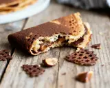Un biscuit croquant au chocolat, garni de crème onctueuse, repose sur un fond de bois rustique. Des éclats de chocolat et des noisettes complètent cette gourmandise.