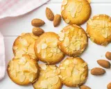 Des biscuits moelleux aux amandes, parsemés d'éclats d'amandes, sur un fond blanc avec une serviette à carreaux roses.