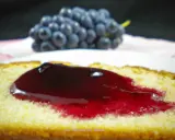 Tranche de gâteau moelleux nappée d'une généreuse gelée de raisin, avec une grappe de raisins bleus en arrière-plan.