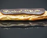 Un délicieux éclair au chocolat, garni de petits éclats dorés, repose sur une surface réfléchissante.