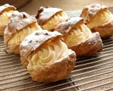 Pâte à choux au robot, garnies d'une crème onctueuse et saupoudrées de sucre glace, refroidissent sur une grille.