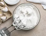 Meringue aérienne, blanc en neige, prête pour une recette gourmande. Des coquilles d'œufs vides à côté témoignent du travail.