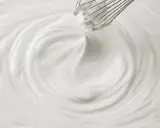 Un fouet mélangeant une crème chantilly aérienne, créant des tourbillons doux et onctueux.